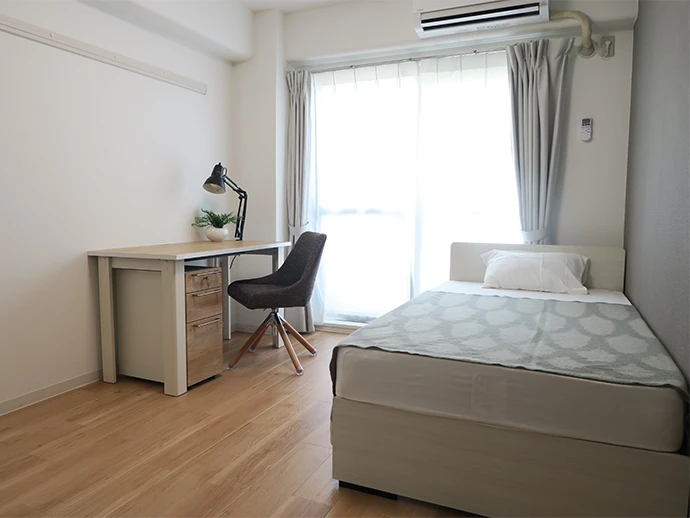 日本郵船の女子社員寮の一室。室内には一人暮らしに必要な設備や家電、デスクやベッドなど必需品を完備（写真のフェイクグリーンとブランケットは撮影用）。全てワンルームタイプで45室。入寮者が自由に利用できる談話室もあり